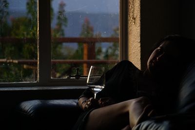 Woman with drink sitting against window at home