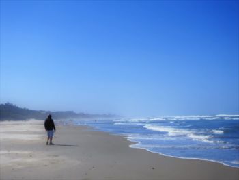 Rear view of man standing on beach against clear blue sky