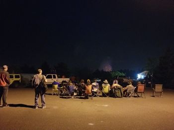 People at illuminated city street against sky at night