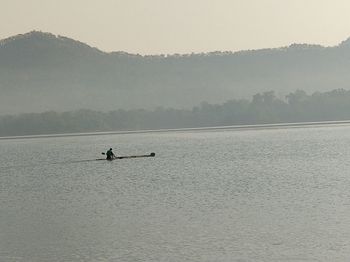 Silhouette man on boat in lake against sky