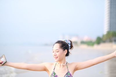 Portrait of young woman with arms raised against sky