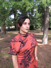Portrait of beautiful woman standing by tree trunk
