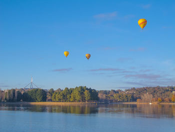 Hot air balloons flying over river against sky