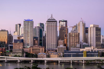 Modern buildings by river against sky in city