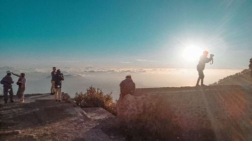 People standing on shore against bright sun