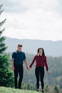 Full length of young couple holding hands while walking on field against sky during sunny day