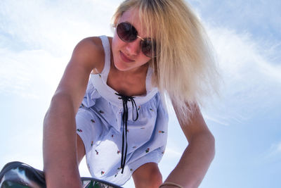 Low angle portrait of young woman wearing sunglasses while bending against sky
