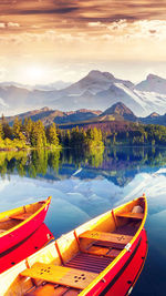 Boats moored by lake against sky during sunset