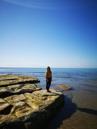 Man standing on rock by sea against clear sky