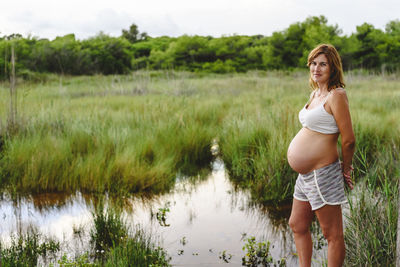 Portrait of pregnant woman standing against grassy land