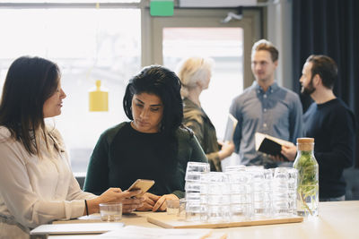 Businesswomen using smart phone at table in brightly lit office