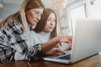 Mother assisting daughter in using laptop on table at home