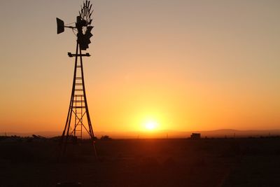 Silhouette cranes on field against sky during sunset