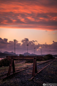 Railroad track amidst field against sky during sunset