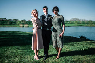 Portrait of friends standing by lake against sky