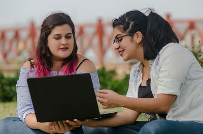 Friends working on laptop at park