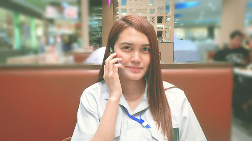 Portrait of smiling woman talking on mobile phone while sitting at restaurant