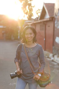 Portrait of smiling woman standing outdoors with her camera 