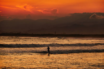 Silhouette man on sea against sky during sunset