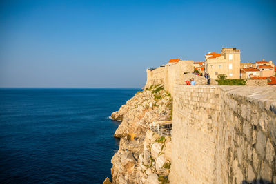 Built structure by sea against clear blue sky