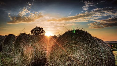 Hay bales on field against sky during sunset