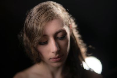 Close-up of young woman looking down against black background