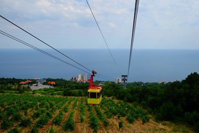 Overhead cable car on field by sea against sky