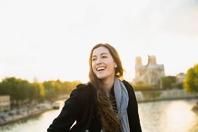 Portrait of smiling young woman standing against river