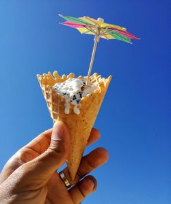 Close-up of hand holding ice cream against blue sky