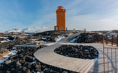 Full frame view of a winding boardwalk in foreground with lighthouse and mountains in background