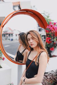 Portrait of beautiful young woman standing by road mirror