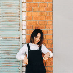 Portrait of young woman standing against wall