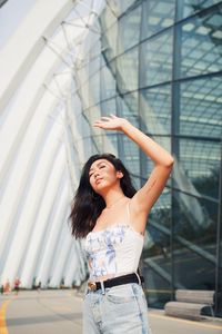 Young woman shielding eyes standing against building in city