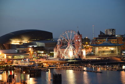 Illuminated city by river against clear sky at night