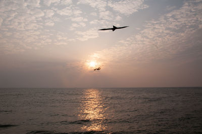 Silhouette airplane flying over sea against sky during sunset