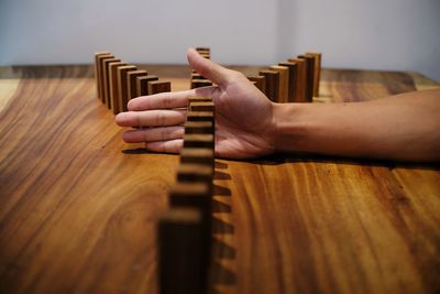 Cropped hand of person blocking wooden dominoes on table