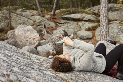 Woman lying on rocks and using smart phone