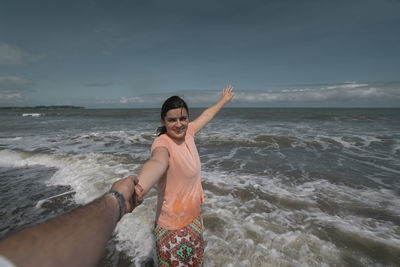 Young hispanic woman holding her partner's hand at the beach wearing pink dress with  background sea