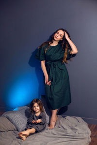 Mother and daughter in dresses sitting on a bed in a bedroom with a blue wall