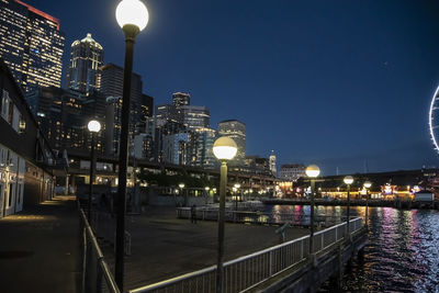 Illuminated buildings by river against sky at night