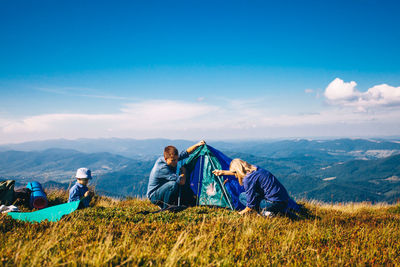People relaxing on mountain against blue sky