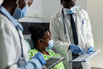 Midsection of doctors wearing mask examining patient at hospital