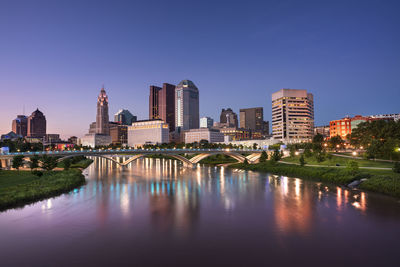 Bridge over river by buildings against clear sky