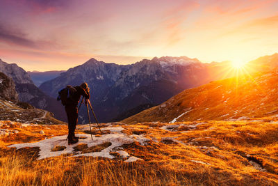 Rear view of man standing on mountain against sky during sunset