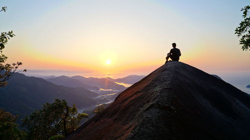 Rear view of man standing on mountain against sky during sunset