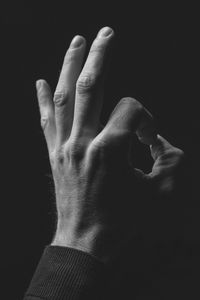 Close-up of man hand gesturing ok sign against black background