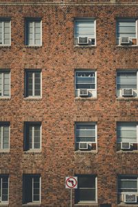 Brick building with lots repetitive patterned  windows with a no left turn sign in front of it