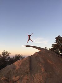 Low angle view of man jumping on rock against blue sky