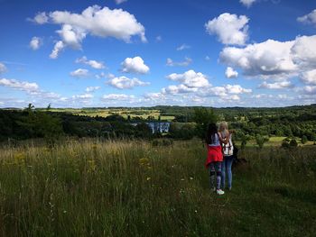 Rear view of female friends standing against sky on field