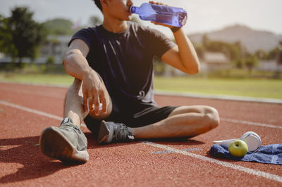 Man drinking water while sitting on running track